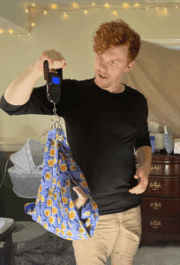 A man holding up a cell phone and a blue bag.