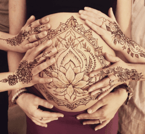 A woman is holding her belly with henna tattoos on it.